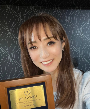 IBJ AWARDの表彰状を手に笑顔の女性