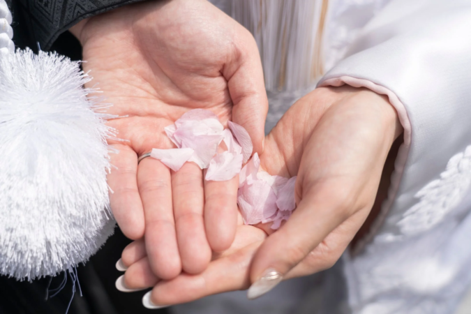 夫婦の手が桜の花びらを優しく包み込んでいるクローズアップ。結婚式や春の慶事を思わせる、美しく感動的な瞬間を捉えています。