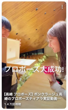 男性が女性に箱を差し出し、女性が花束を持って笑顔で応じているプロポーズの瞬間
