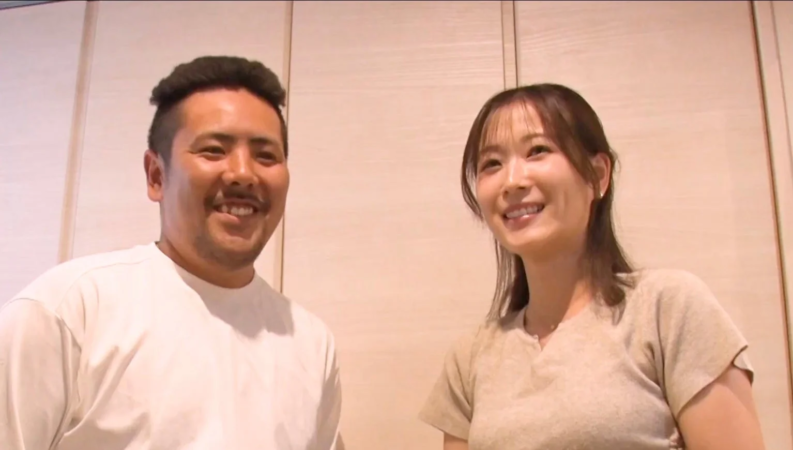 笑顔の男女が並んで写っている写真です。二人は楽しそうに微笑んでおり、親密な雰囲気が伝わってきます。シンプルな背景の室内で撮影されたポートレートです。
