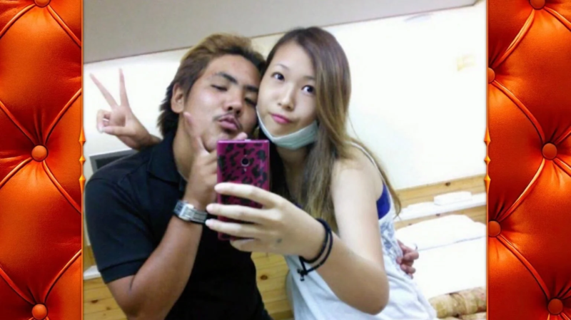 若いカップルがスマートフォンで自撮りをしている。男性はキス顔とピースサインをしており、女性はマスクを顎に下げてカメラを構えている。室内での仲睦まじい瞬間を捉えた写真。